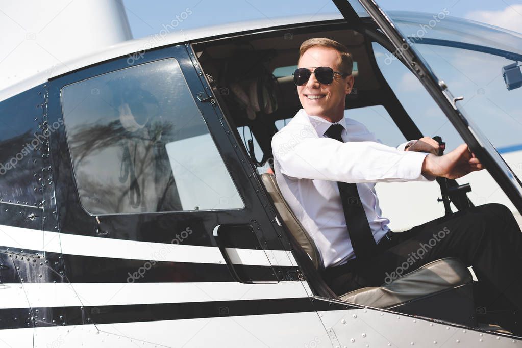 good-looking Pilot in formal wear and sunglasses sitting in helicopter cabin