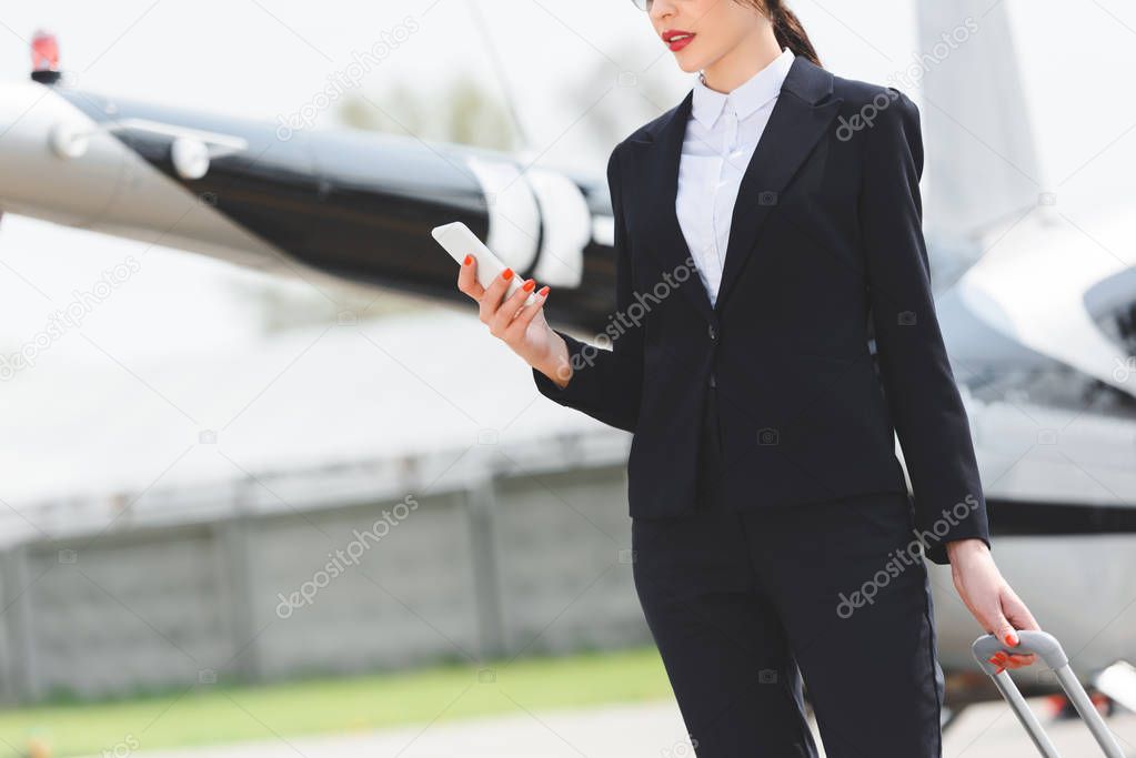 Cropped view of businesswoman in formal wear using smartphone near helicopter