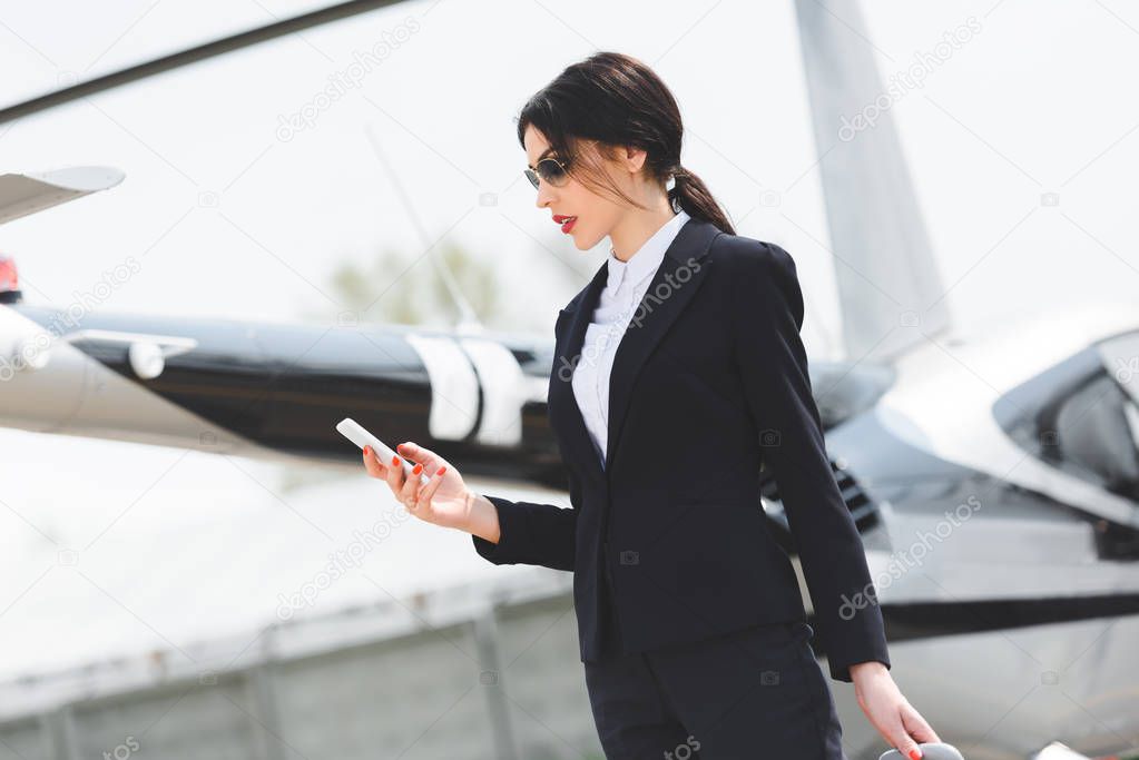 businesswoman in formal wear using smartphone near helicopter