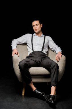 yakışıklı adam kameraya bakıyor ve siyah koltukta oturuyor 