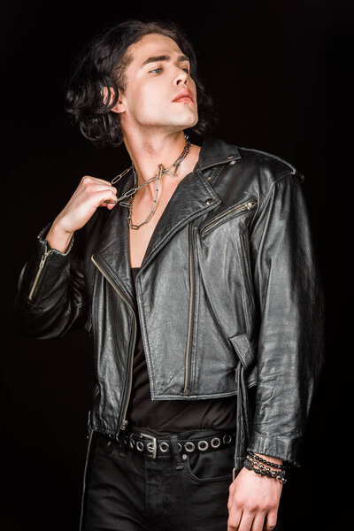 serious man touching chains on neck while standing isolated on black 