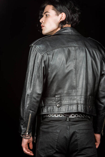 serious man in leather jacket standing isolated on black  