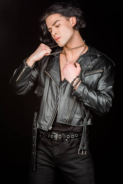 confident man touching neck chains while standing isolated on black 