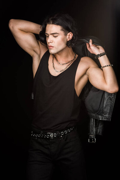 Красивый мужчина, держащий кожаную куртку и стоящий изолированный на черном
 