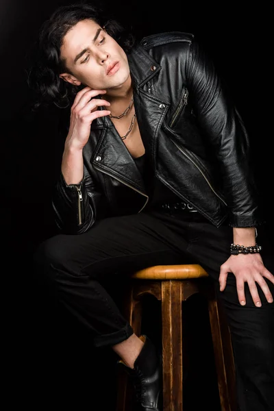 pensive man in leather jacket sitting on chair isolated on black