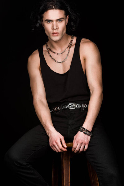 красавчик, сидящий на деревянном стуле, изолированном на черном
 