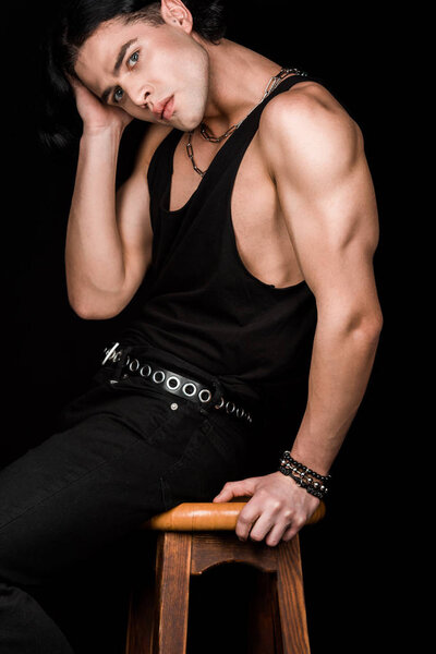handsome young man sitting on wooden chair isolated on black 