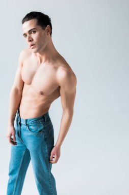yakışıklı kaslı adam kameraya bakıyor ve beyaz kot duruyor 