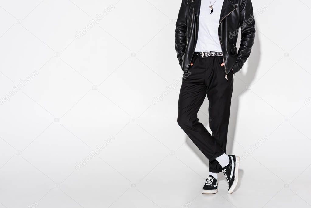 cropped view of man in leather jacket standing with crossed legs on white 