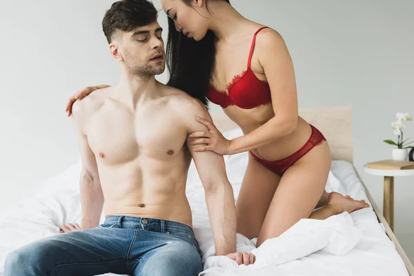 有吸引力的女人在红色内衣拥抱英俊的无衬衫男友在卧室 — 图库照片