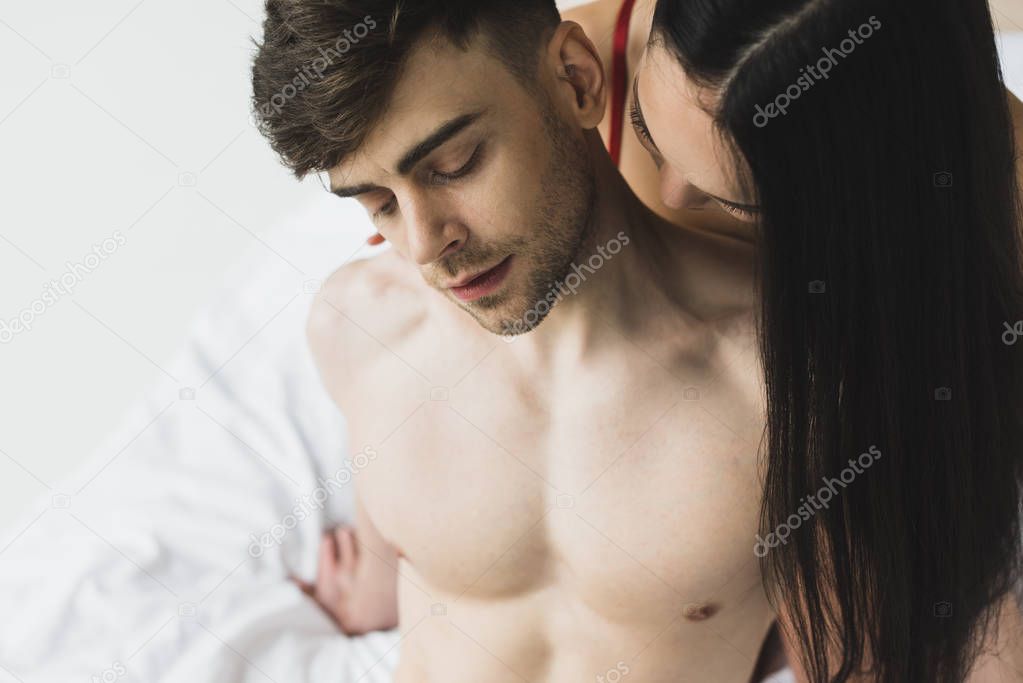 asian woman kissing neck of handsome shirtless boyfriend