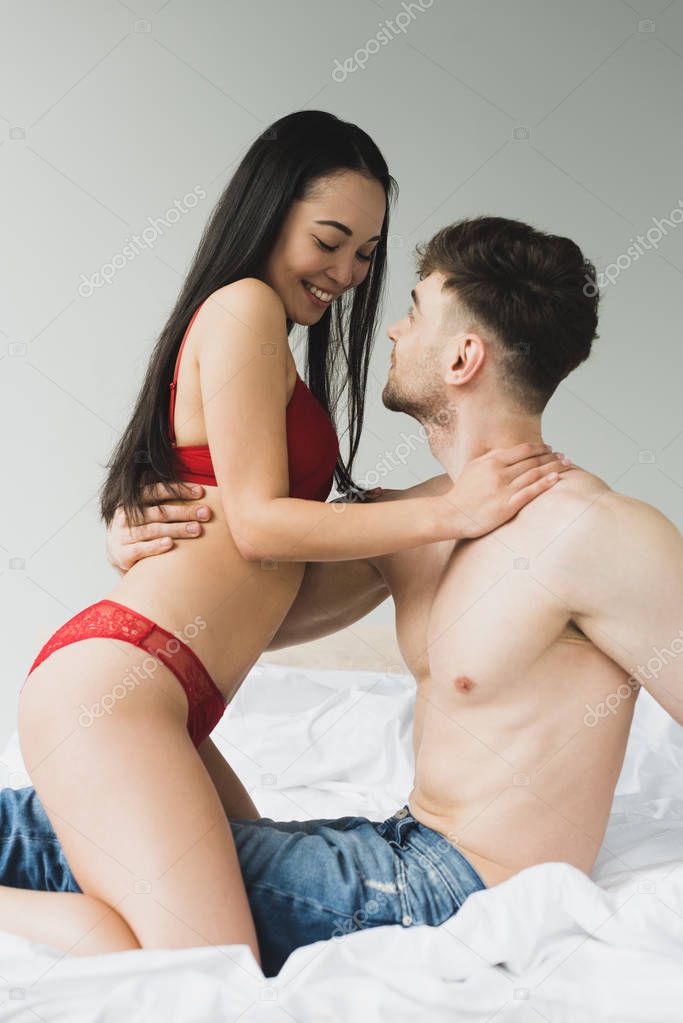 happy interracial couple in underwear smiling and hugging in bedroom