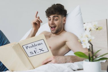 smiling man showing idea sign while reading problems in sex book  clipart
