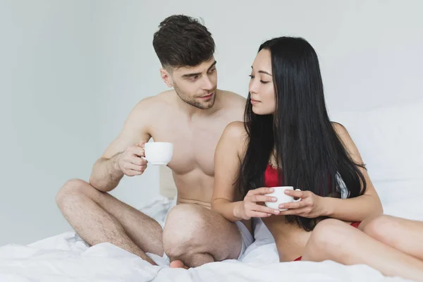 Smiling Interracial Couple Sitting White Bedding Holding Coffee Cups — Stock Photo, Image