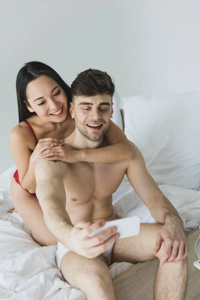Happy Interracial Couple Underwear Sitting White Bedding Taking Selfie Smartphone — Stock Photo, Image