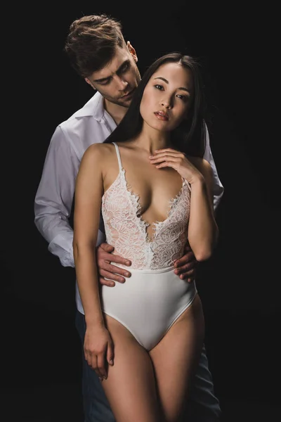 白いシャツのハンサムな男は 黒で孤立した白いランジェリーでセクシーなアジアのガールフレンドにキスして抱きしめる — ストック写真
