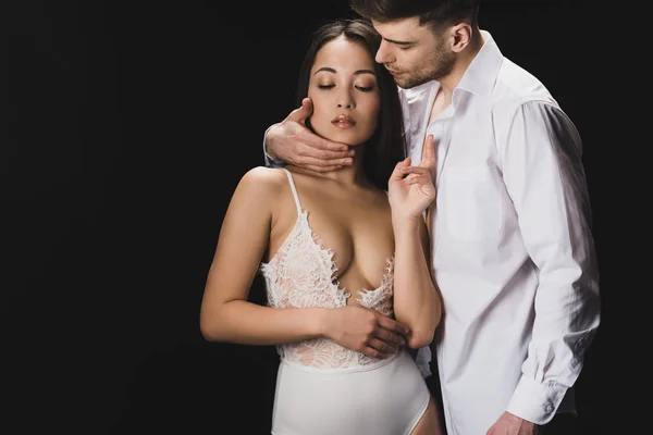 黒で隔離された白いランジェリーでセクシーなアジアのガールフレンドを抱きしめるハンサムな若者 — ストック写真