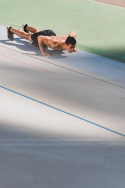 shirtless mixed race sportsman doing push ups at stadium clipart