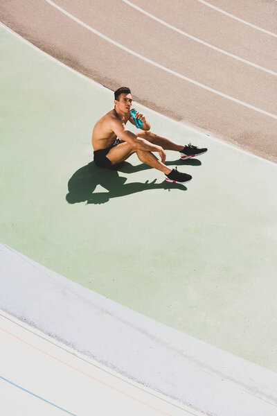 mixed race sportsman sitting at stadium and drinking water