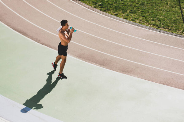 overhead view of mixed race sportsman holding towel and drinking water at stadium