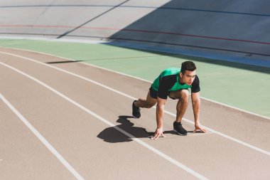 mixed race sportsman preparing to run at stadium clipart