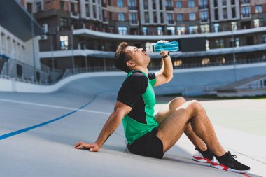 mavi şişeden stadyum ve İçme suyunda koşu pistinde oturan karışık yarış sporcunun yan görünümü 