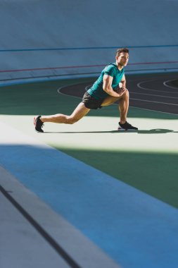 karışık yarış sporcusu stadyumda lunges yapıyor, güneş ışığında yeşil katta ayakta