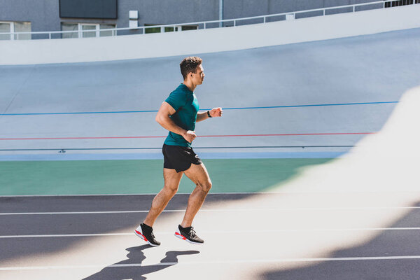 Вид сбоку на смешанные гонки и человека, бегущего по дорожке на стадионе
