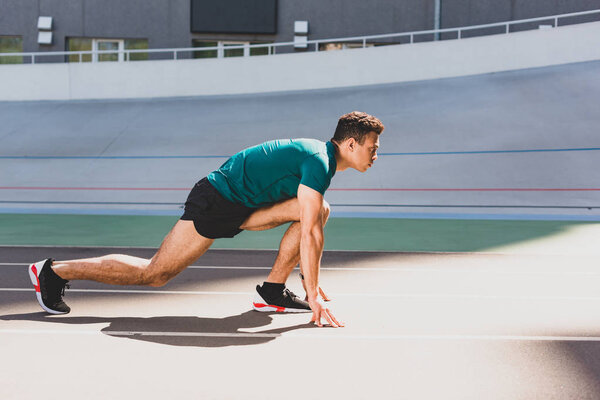side view of mixed race sportsman on start position at stadium looking forward