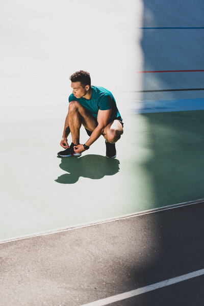 mixed race sportsman lacing up sneakers at stadium