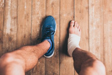 cropped shot of injured sportsman sitting in one sneaker with one foot in elastic bandage clipart