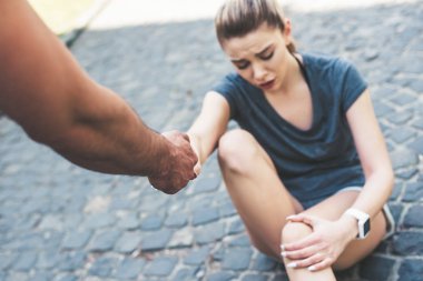 cropped shot of man giving hand to injured sportswoman sitting on pavement  clipart