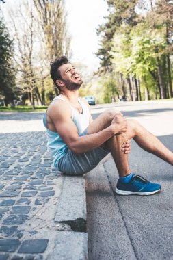 Genç sporcu sınırda oturup yaralı bacağa dokunurken çığlık atıyor.