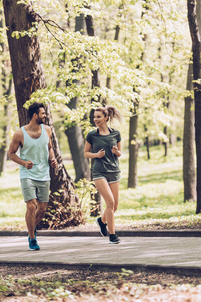 handsome man and pretty woman in sportswear talking while running in park