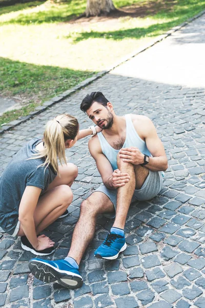 Mujer Joven Ropa Deportiva Tocando Hombro Deportista Lesionado Sentado Pavimento — Foto de Stock