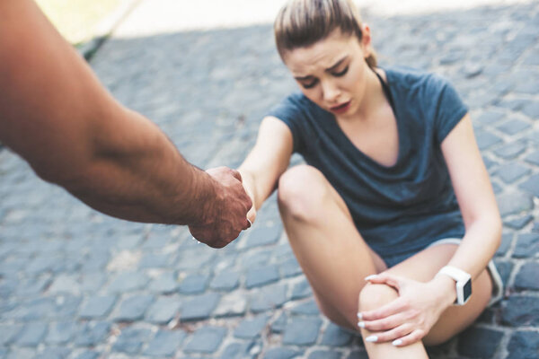 cropped shot of man giving hand to injured sportswoman sitting on pavement 