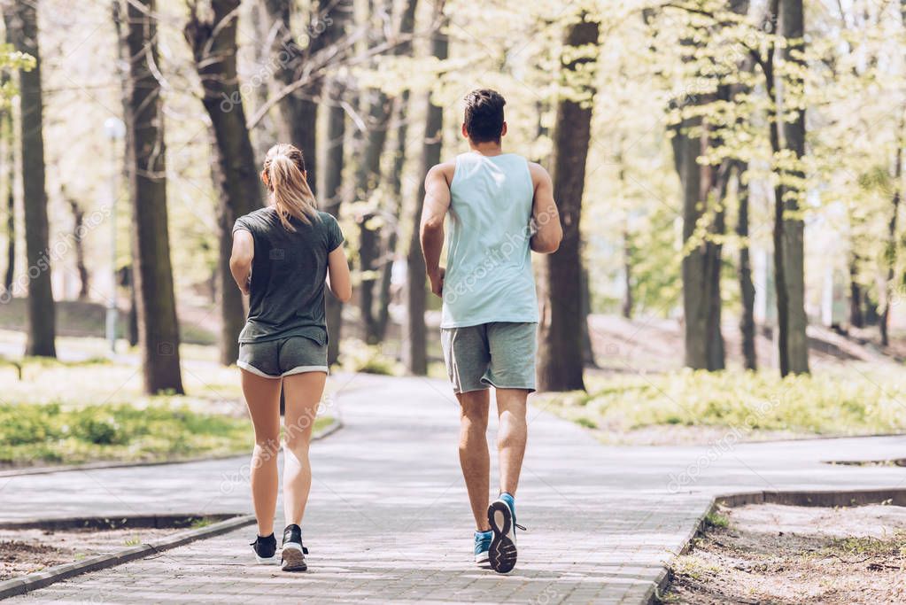 back view of young sportsman and sportswoman running on walkway in park