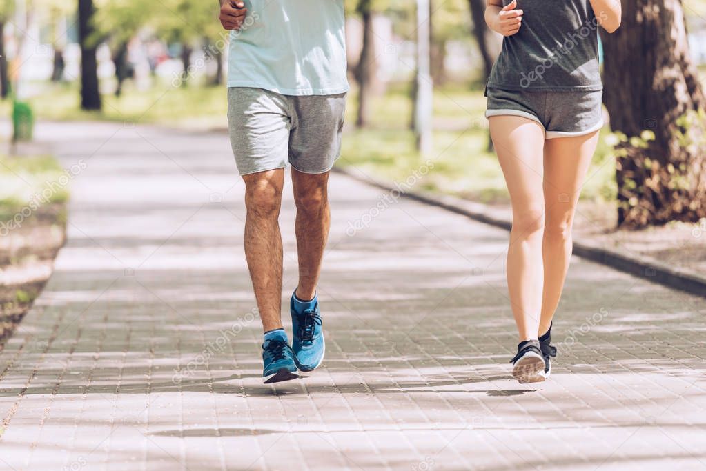 cropped shot of sportsman and sportswoman running along walkway in park