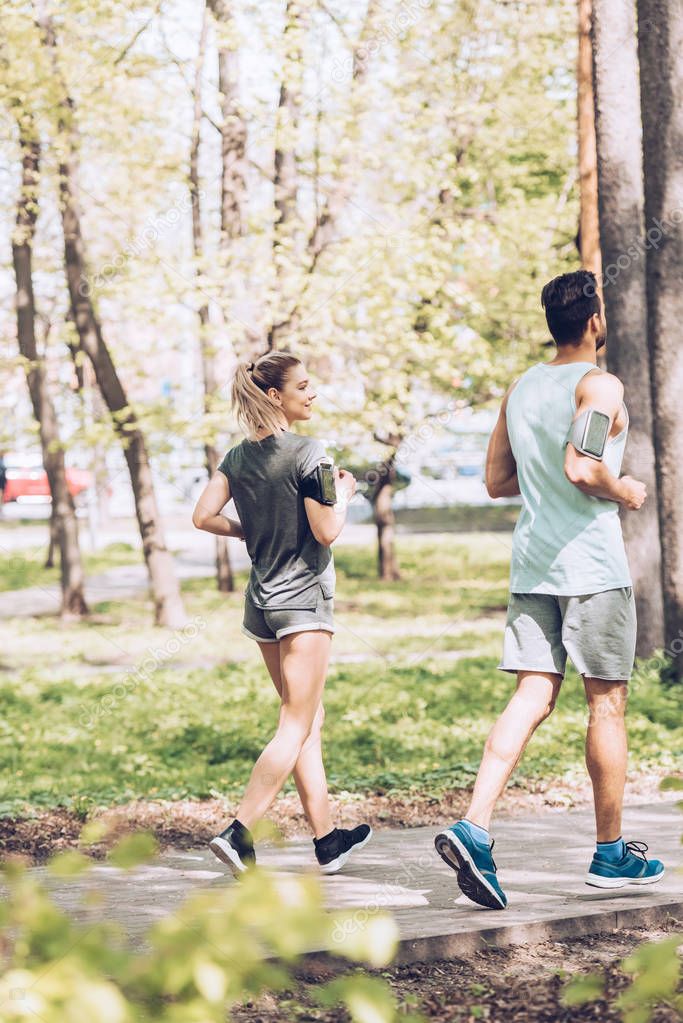 selective focus of young sportswoman and sportsman running together in park