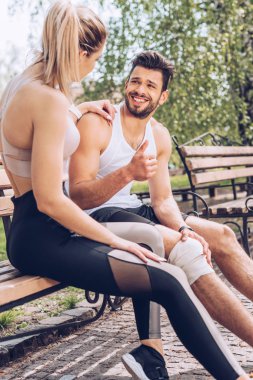 yaralı sporcu gülümseyerek ve sporcu kadın yanında bankta otururken başparmak gösteren