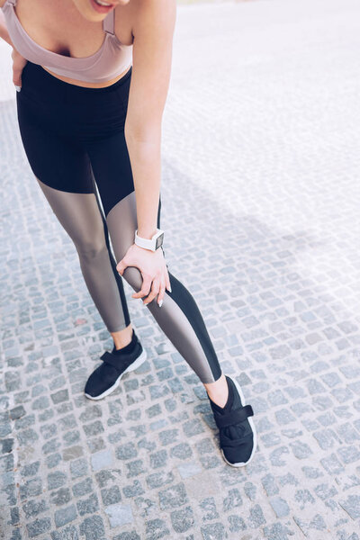 cropped shot of sportswoman standing on pavement and touching injured leg