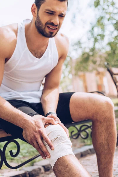 Deportista Molesto Sentado Banco Tocando Vendaje Elástico Rodilla Lesionada — Foto de Stock