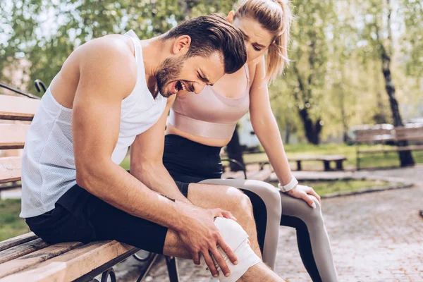 Mladá Žena Sportovním Oblečení Sedí Lavičce Blízkosti Zraněného Sportovce Trpí — Stock fotografie