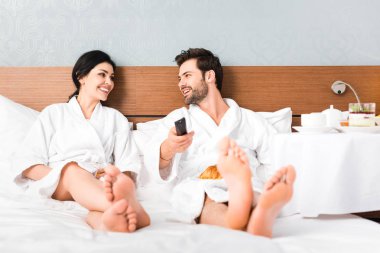 otel odasında kadın bakarken uzaktan kumanda tutan neşeli adam seçici odak 