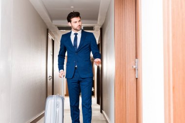yakışıklı adam bagaj ile ayakta ve otel koridorunda otel kartı tutan 