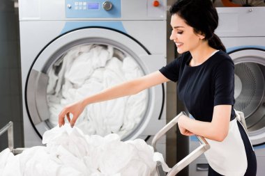 çamaşır makinelerinin yanında dururken çarşaflara bakan neşeli hizmetçi