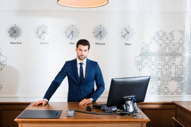 handsome receptionist standing at reception desk in hotel  clipart