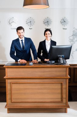 cheerful receptionists in formal wear standing at reception desk  clipart