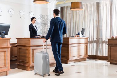 attractive receptionist looking at businessman with luggage  clipart