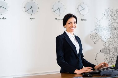 attractive receptionist smiling while standing at reception desk  clipart